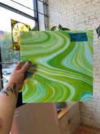 Hand holding a green and white marbled glass sheet against a brick wall.