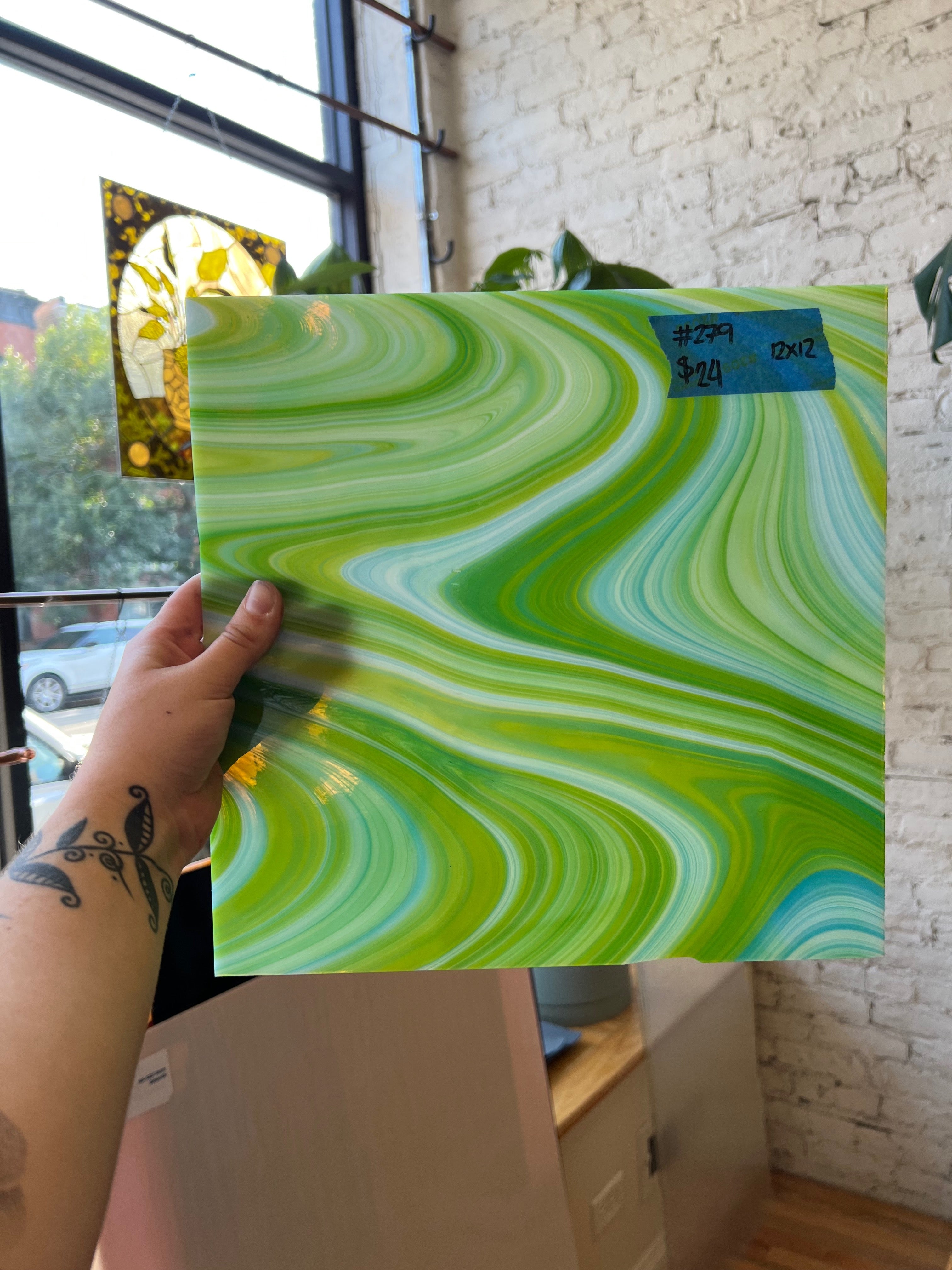 Hand holding a green and white marbled glass sheet against a brick wall.