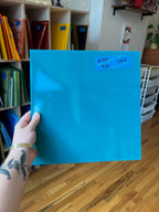 Person holding a blue sheet of glass with a label in a room with shelves and books.