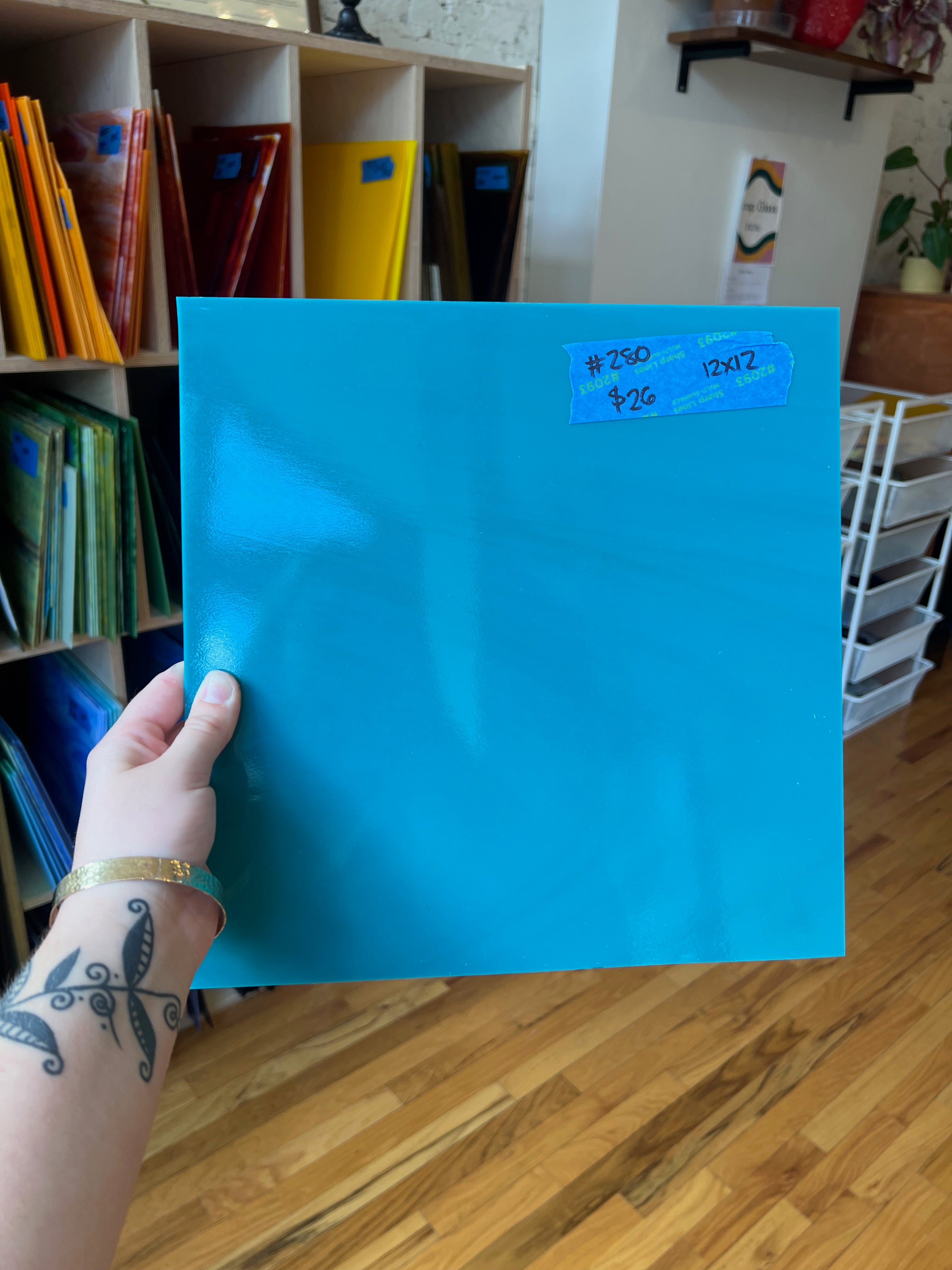 Person holding a blue sheet of glass with a label in a room with shelves and books.