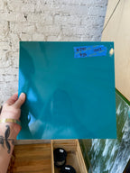 Person holding a large blue sheet of glass with dimensions on a textured wall background