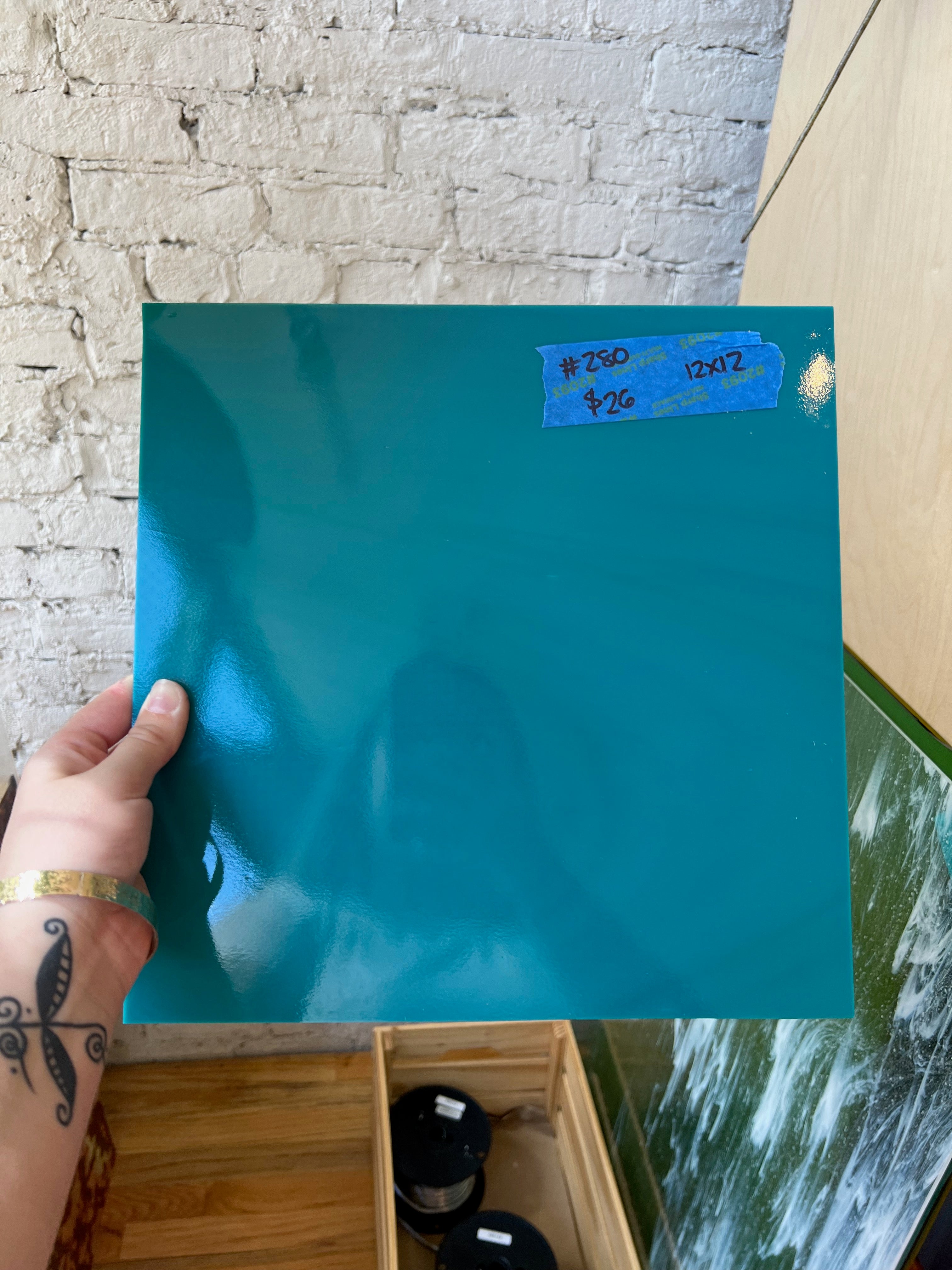 Person holding a large blue sheet of glass with dimensions on a textured wall background