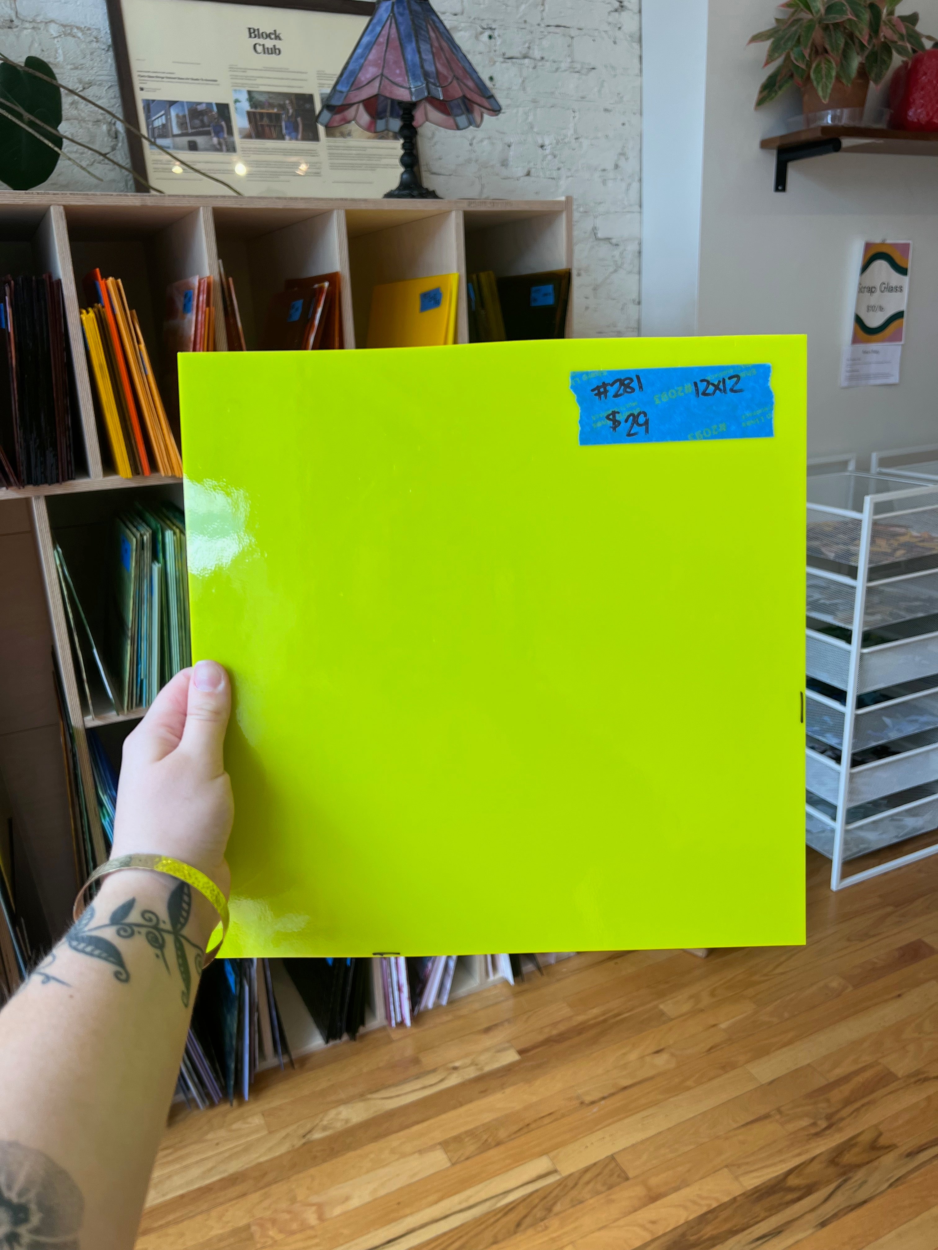 Person holding a bright yellow sheet of glass with blue labels in a room with bookshelves and a lamp.