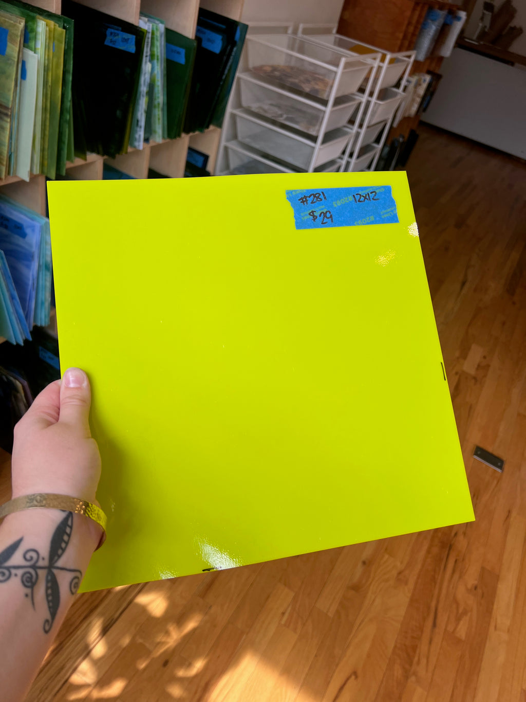 Hand holding a bright yellow sheet of glass with a price tag on a wooden floor.