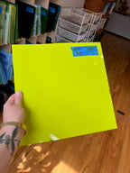 Hand holding a bright yellow sheet of glass with a price tag on a wooden floor.