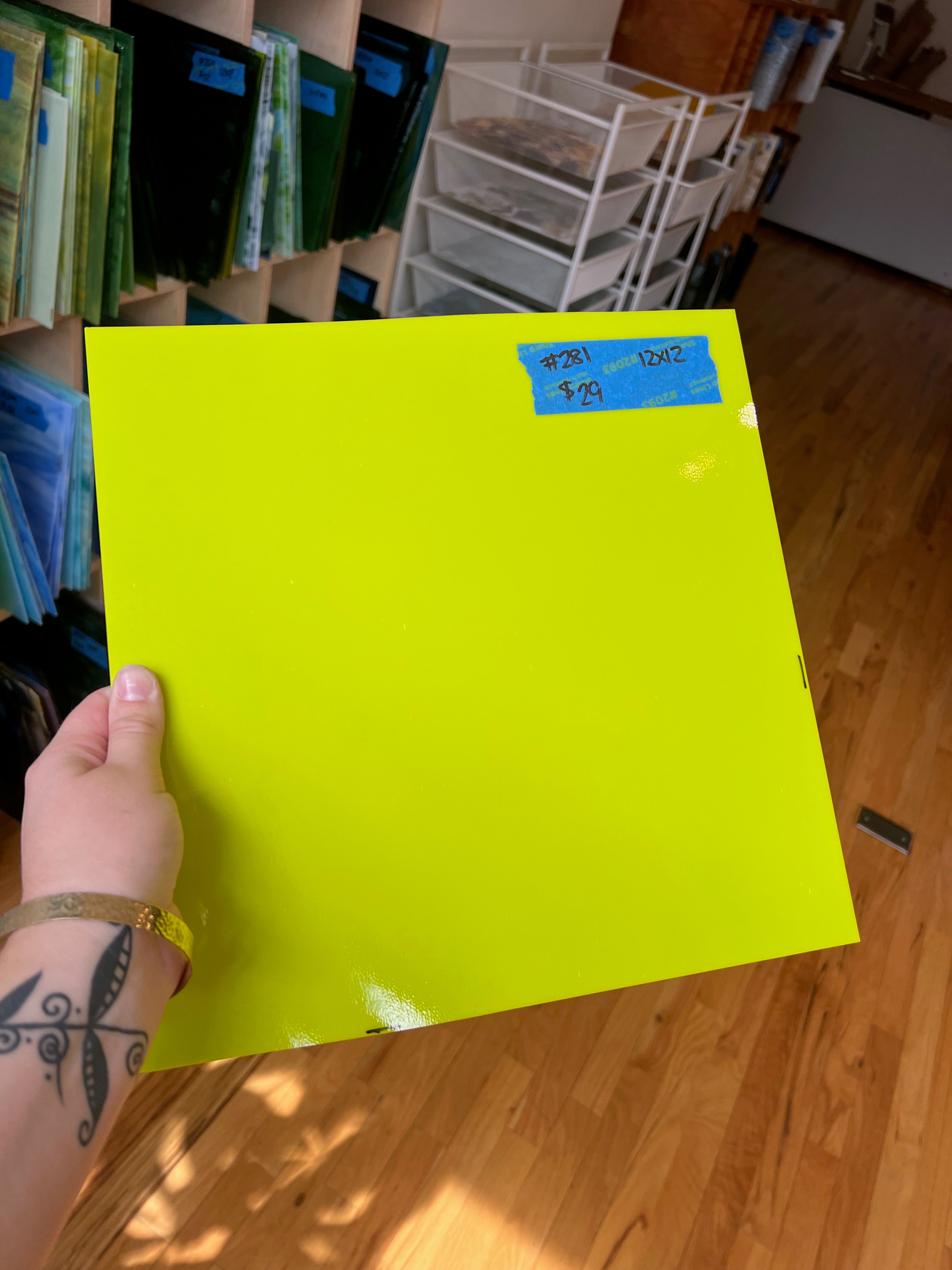 Hand holding a bright yellow sheet of glass with a price tag on a wooden floor.