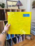 Yellow piece of stained glass held by a person in front of shelves.