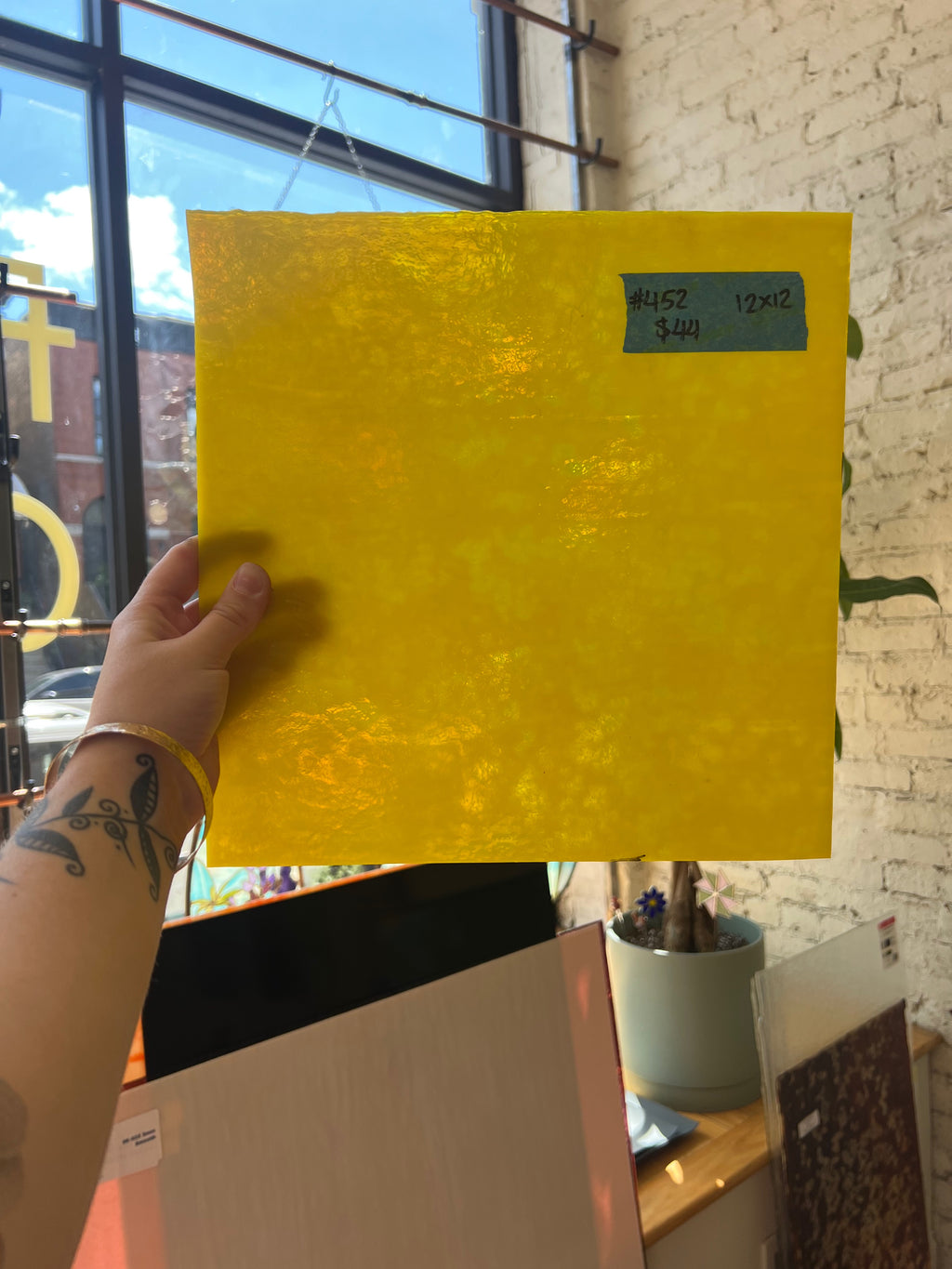 Hand holding a yellow square of stained glass with a price tag in front of a store window.