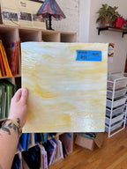 Hand holding a yellow abstract glass sheet with a price tag in an indoor setting.