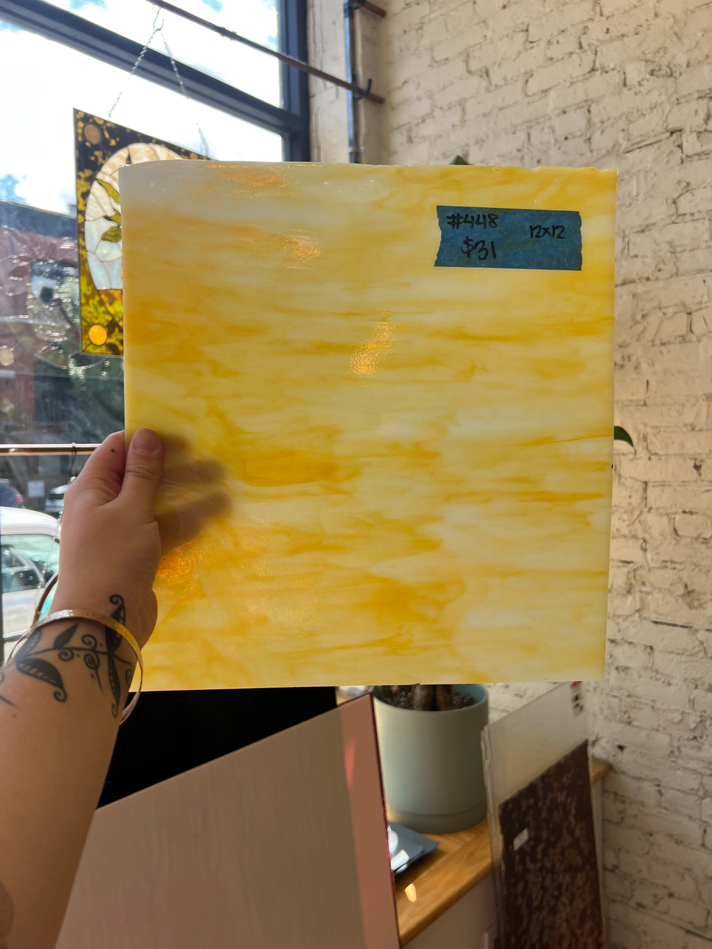 Hand holding a yellow abstract glass sheet against a brick wall.