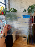 Person holding a rectangular glass panel with blue streaks in an indoor setting.