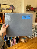 Person holding a textured gray piece of glass with a price tag in a room with shelves.