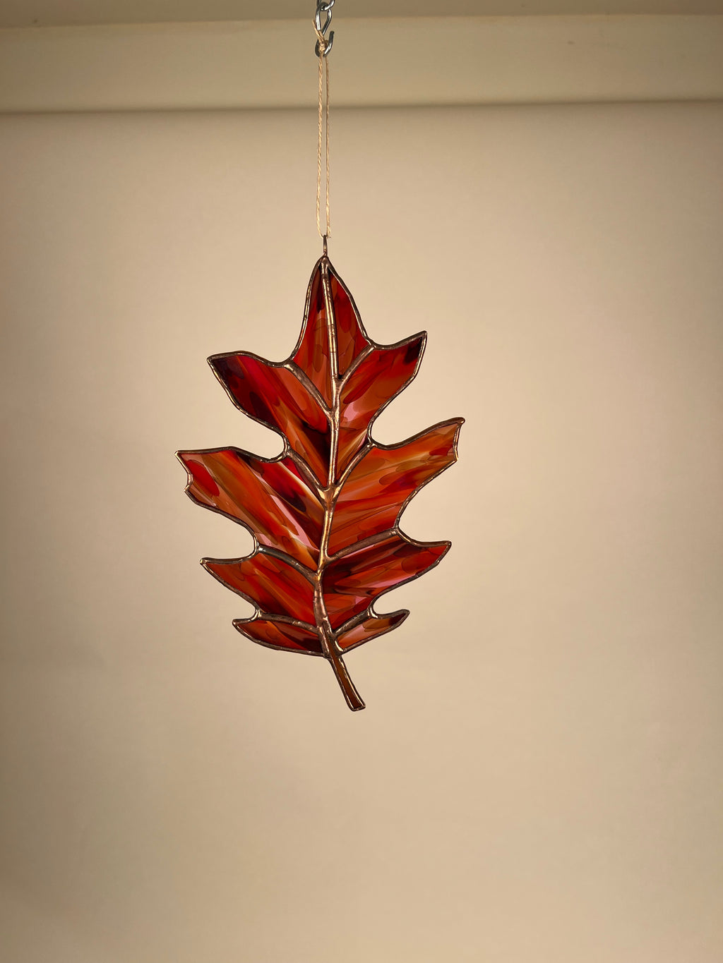Decorative leaf-shaped stained glass ornament hanging against a beige background