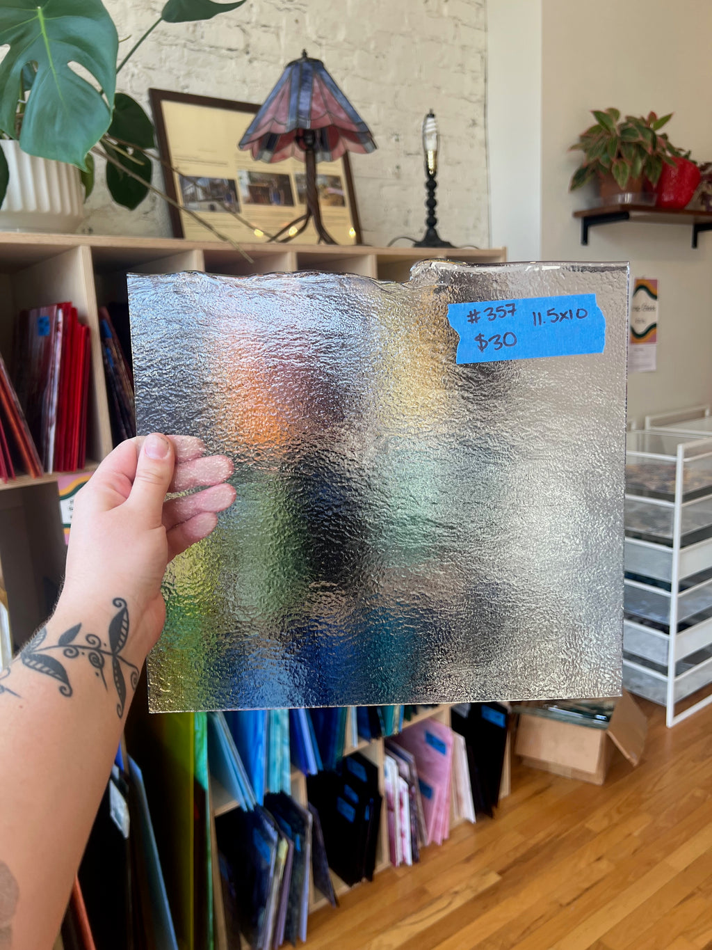 Person holding a sheet of glass with a price tag in a room with shelves and plants.
