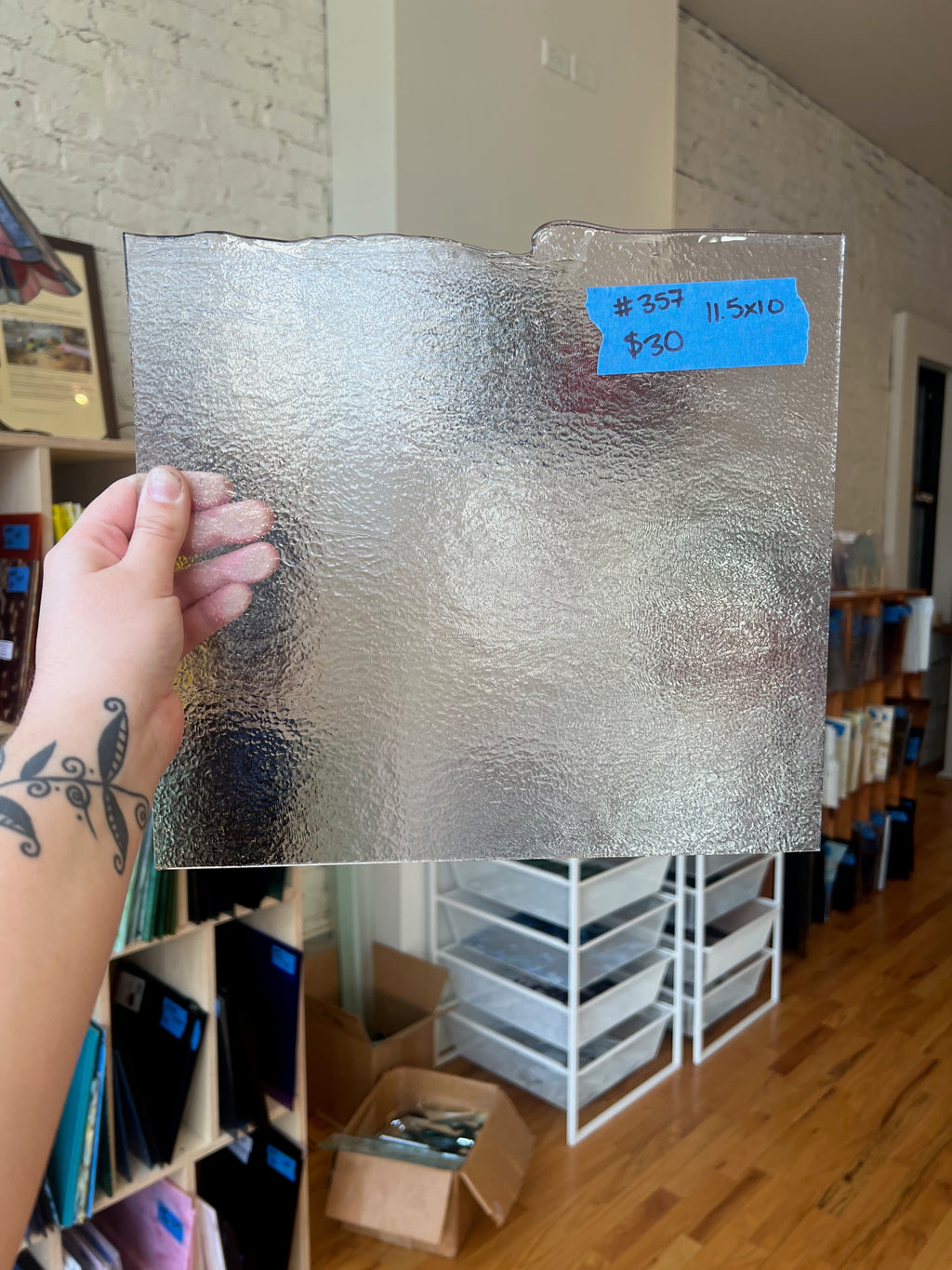 Person holding a sheet of glass with a price tag in a room with storage shelves and boxes.