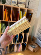Person holding a scrub brush in front of a bookshelf with colorful books.
