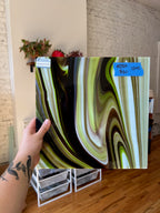 Person holding a piece of decorative glass with swirling patterns in a room.