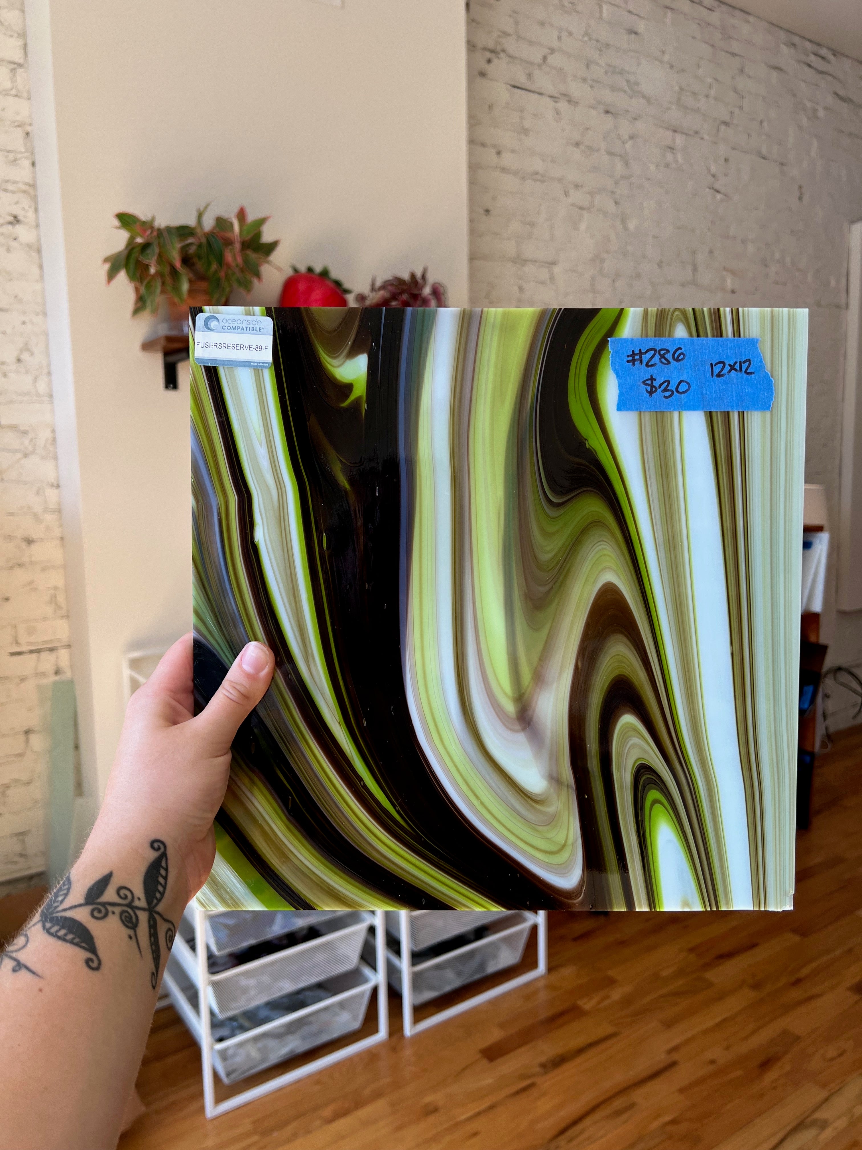 Person holding a piece of decorative glass with swirling patterns in a room.