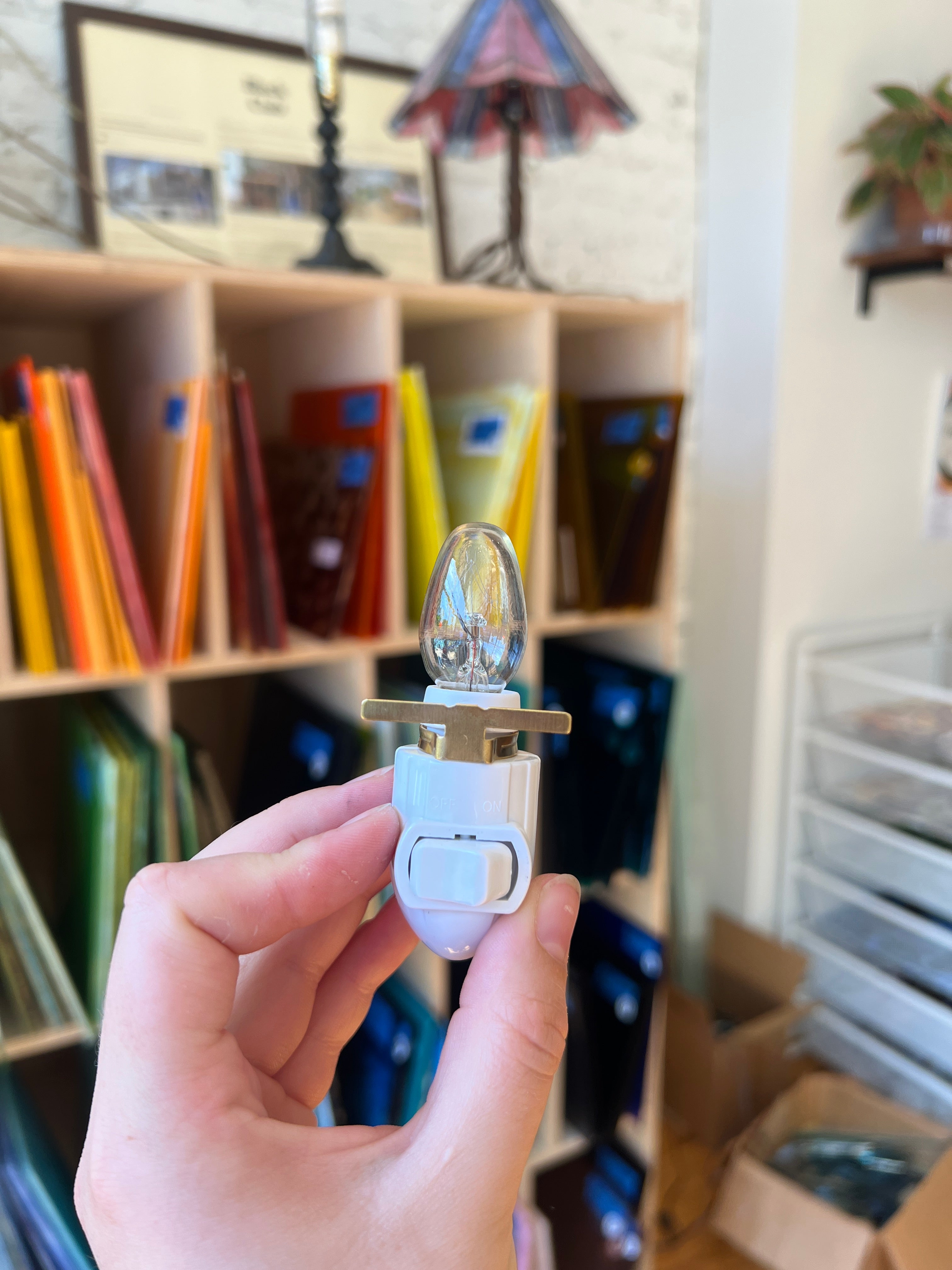 Hand holding a small electronic device with a blurred background of books and stationery.