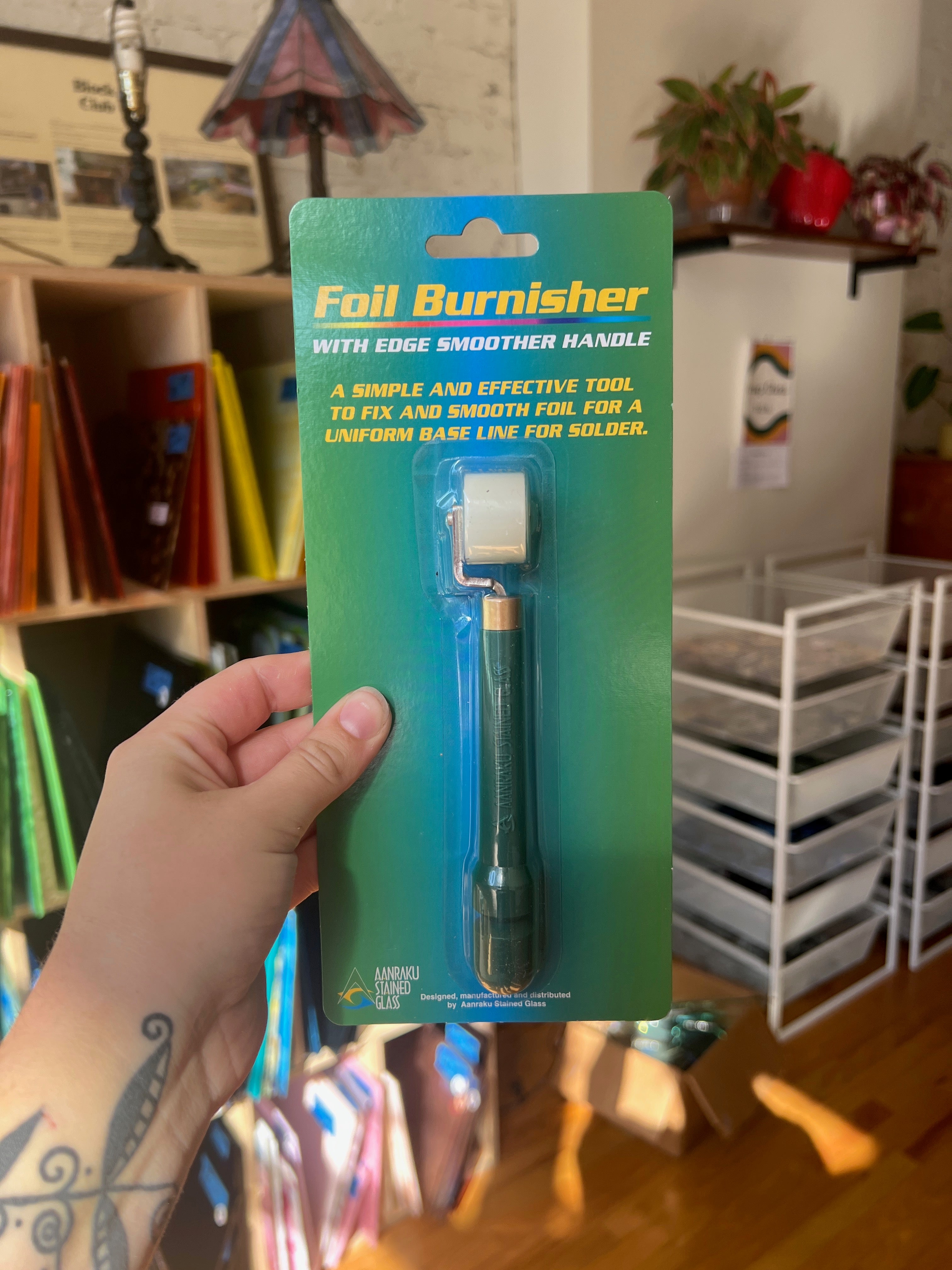 Foil Burnisher on a green card held in a hand with a room background