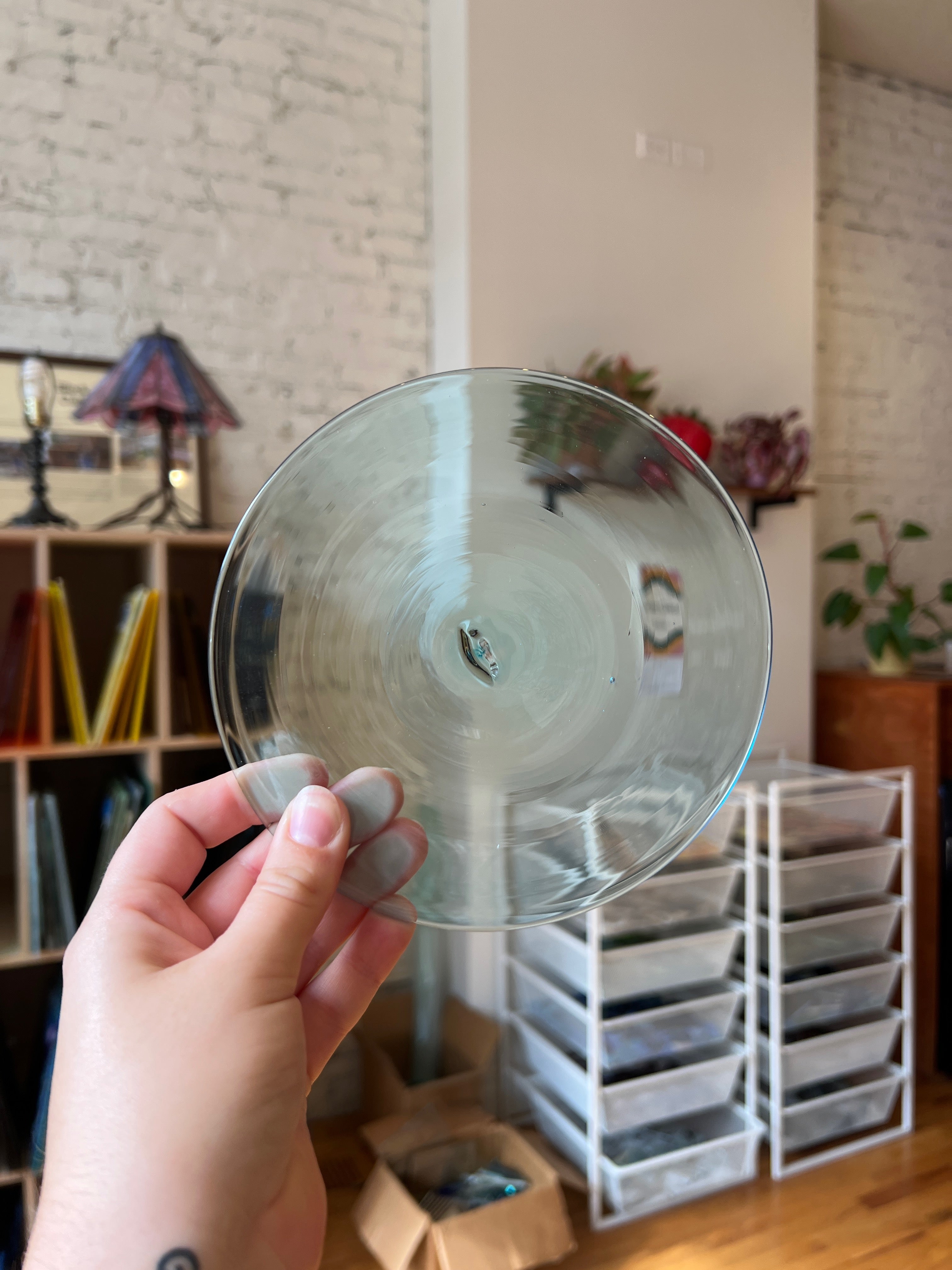 Hand holding a clear glass rondel with a blurred indoor background