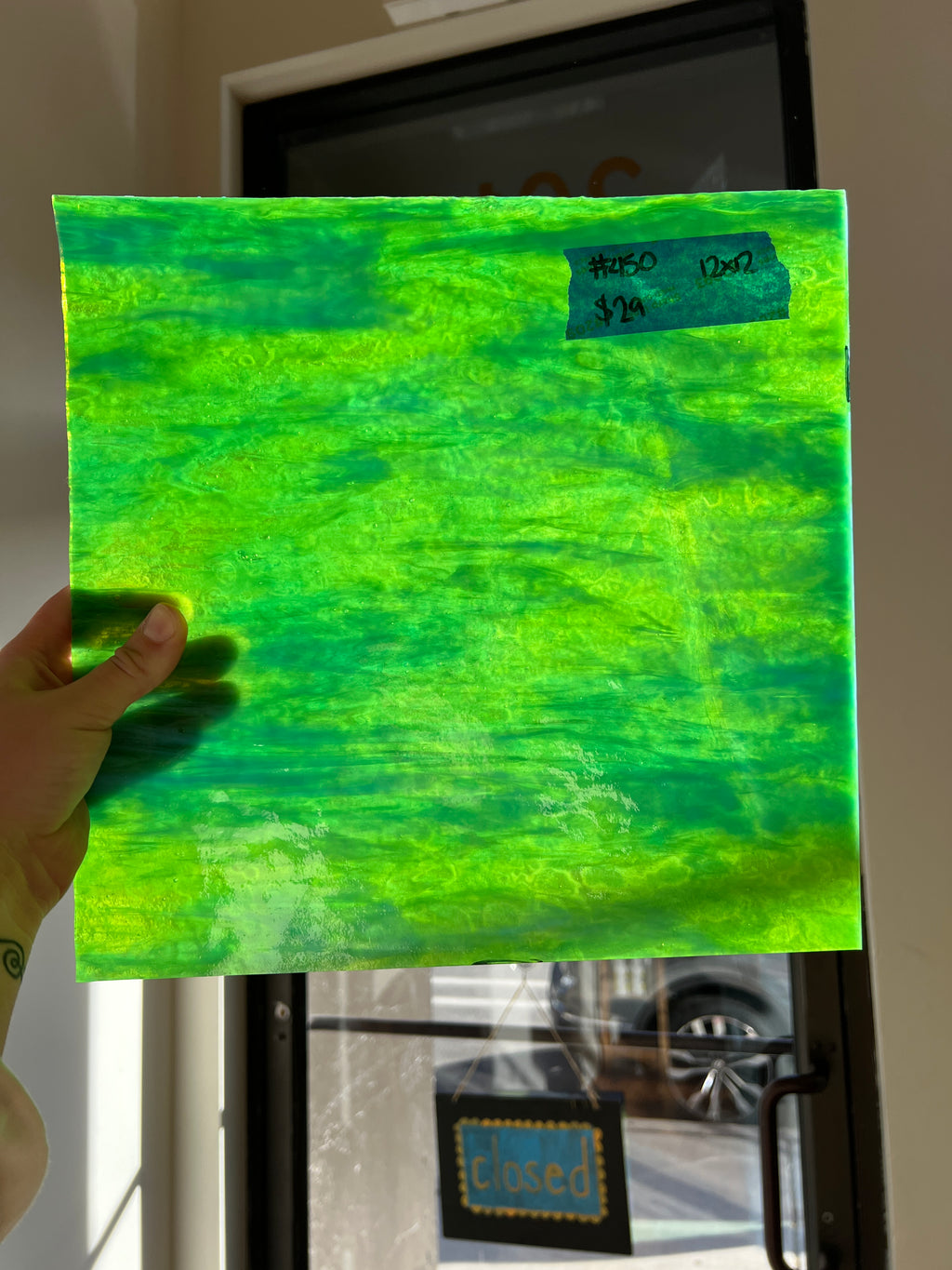 Hand holding a green textured glass sheet with a blurred background