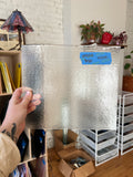 Person holding a textured piece of glass with a blue label in an indoor setting