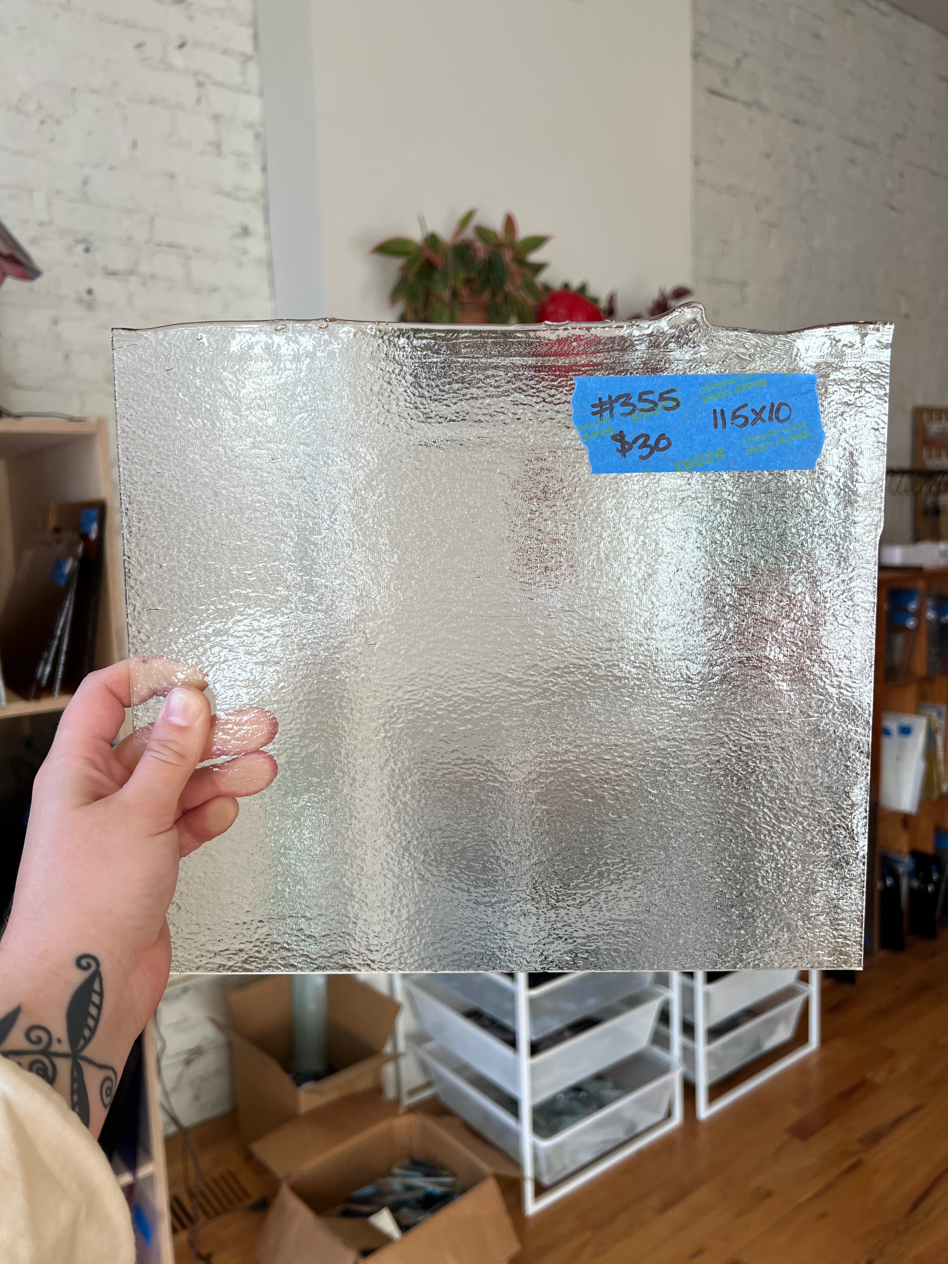 Person holding a square piece of stained glass with a blue label in an indoor setting.