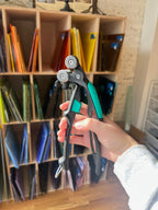 Hand holding a mosaic cutter in front of a bookshelf with colorful books