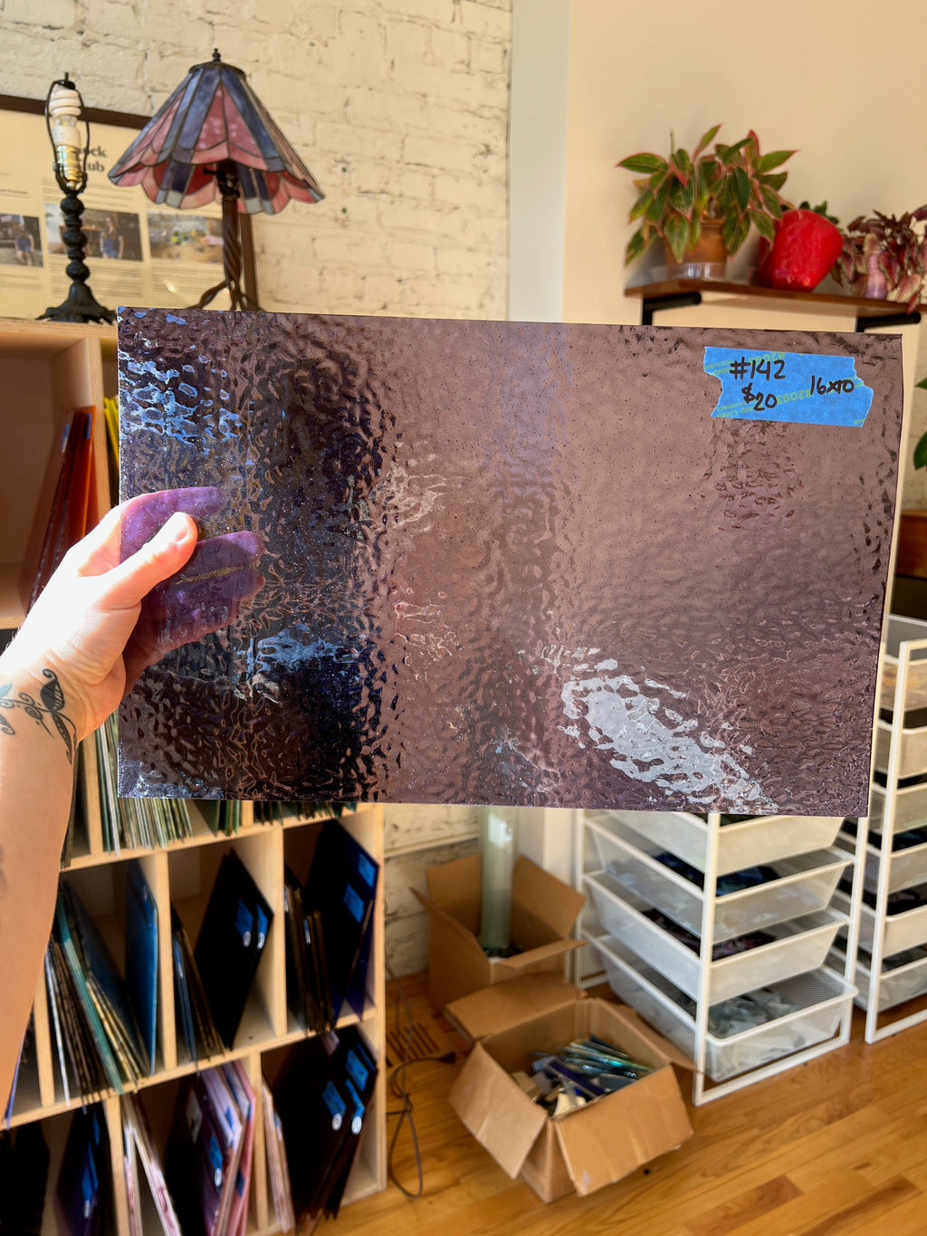 Person holding a textured lilac glass sheet in a room with shelves and decor