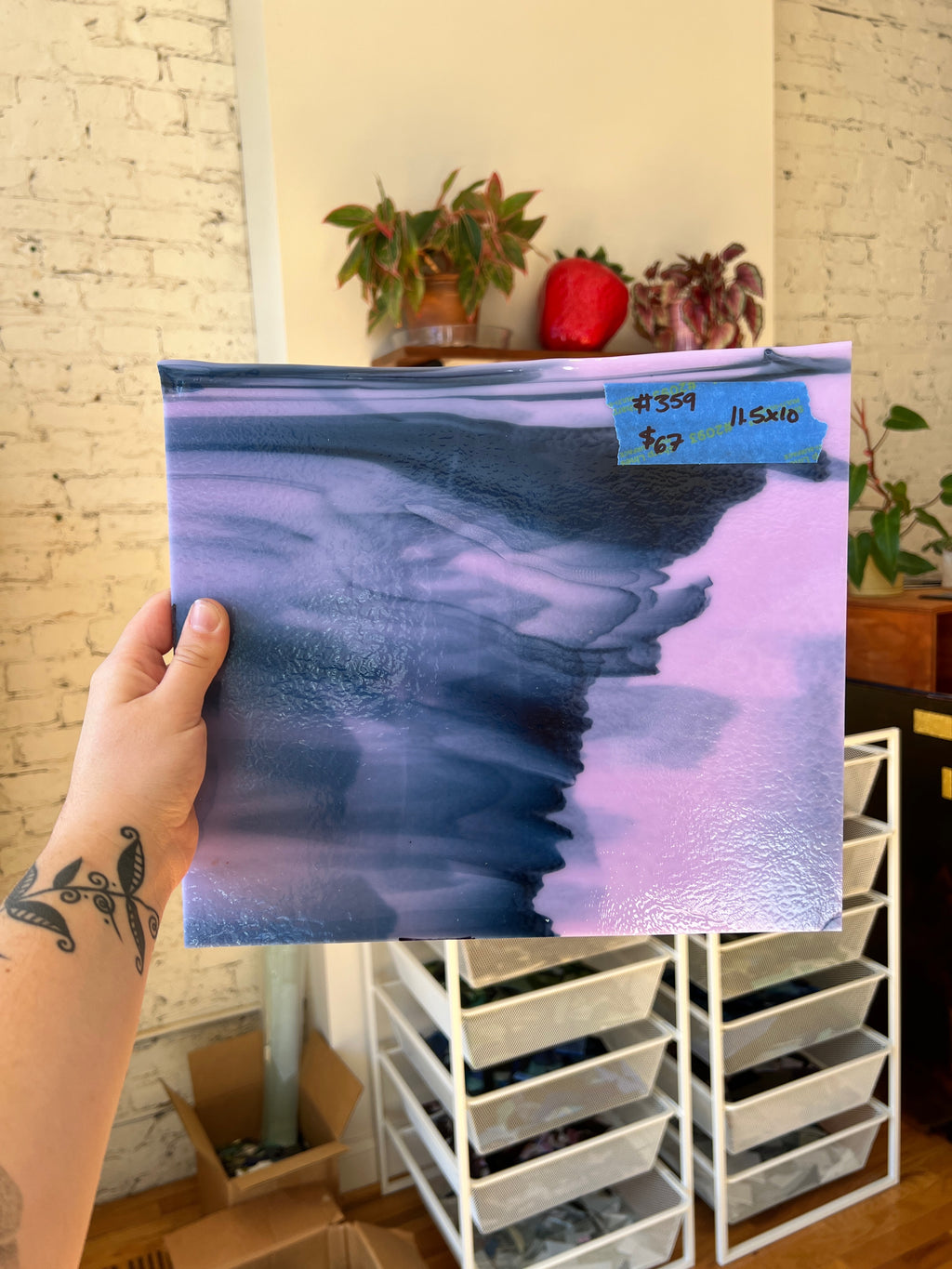 Person holding a blue and purple abstract piece of stained glass in front of a brick wall.