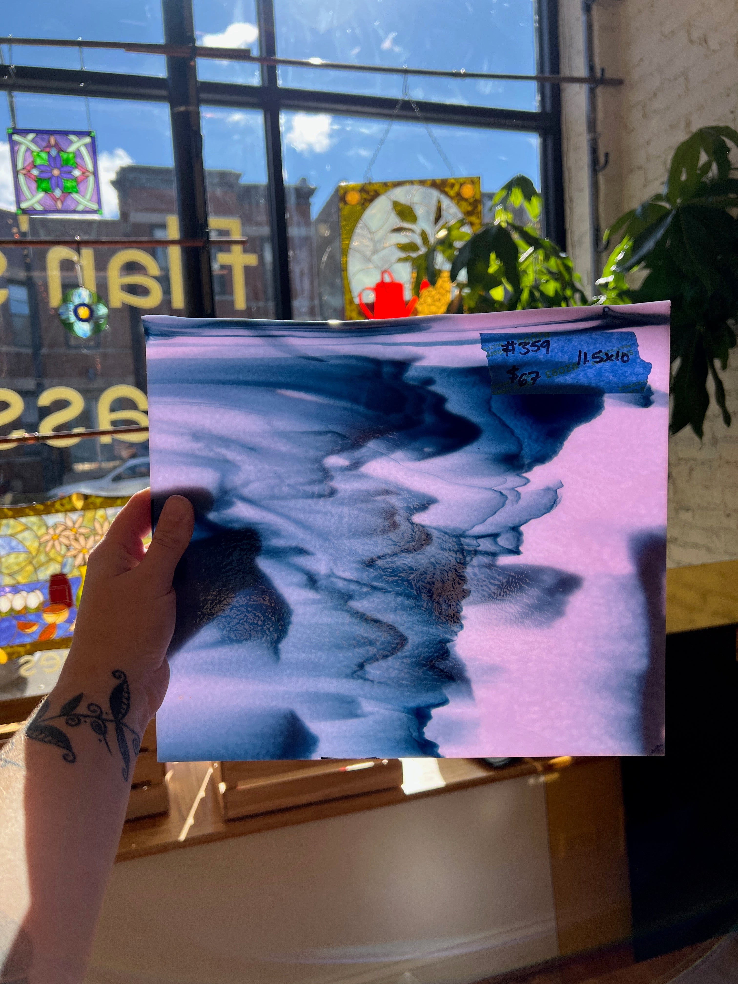 Person holding a piece of glass with a blue and pink abstract design in front of a store window.