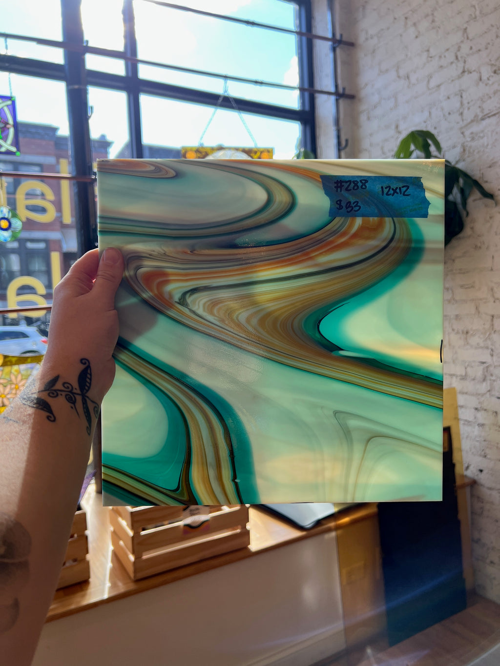 Person holding a piece of glass with a colorful abstract pattern in front of a window.