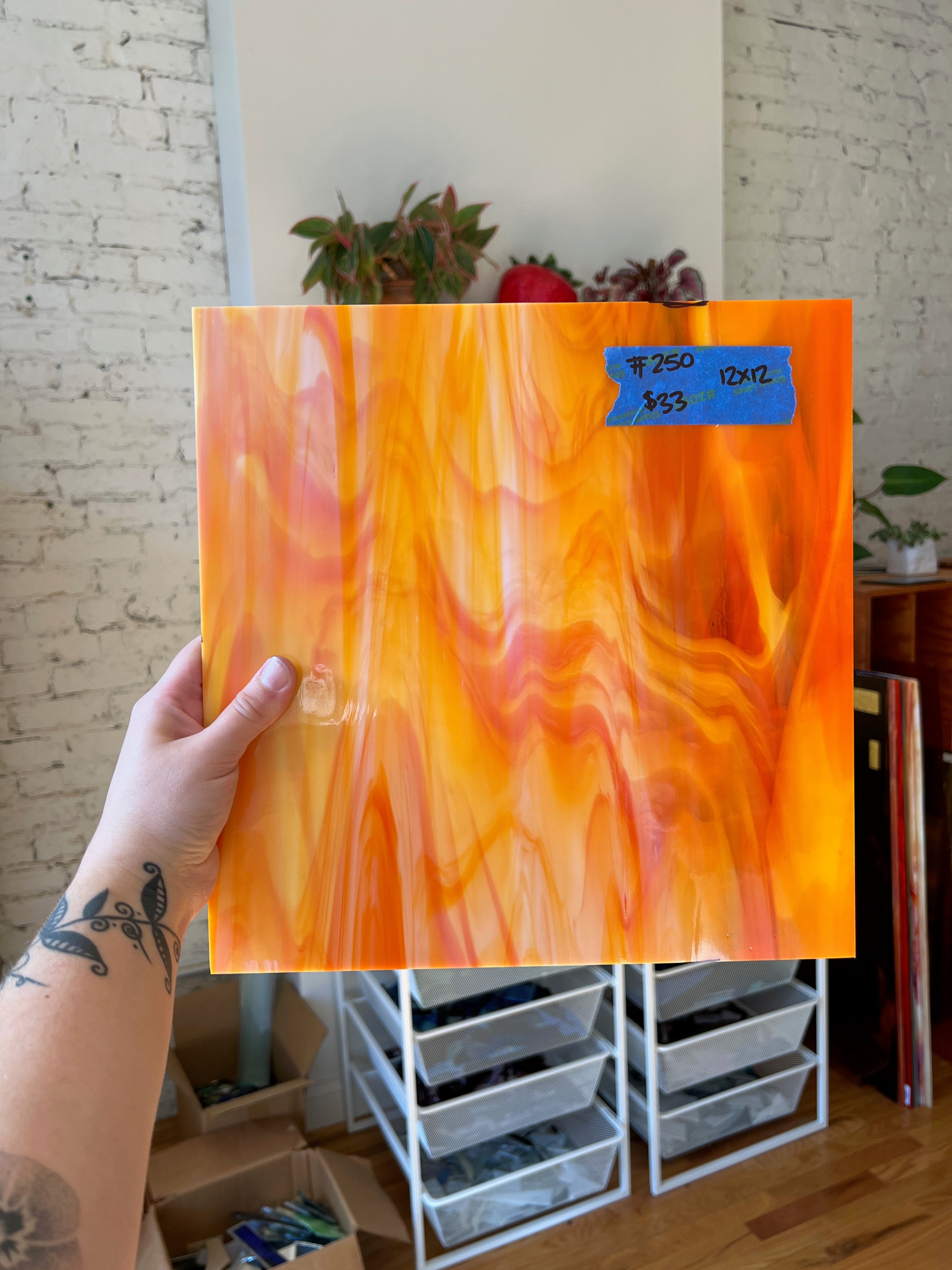 Hand holding an orange swirled piece of glass against a brick wall background. 