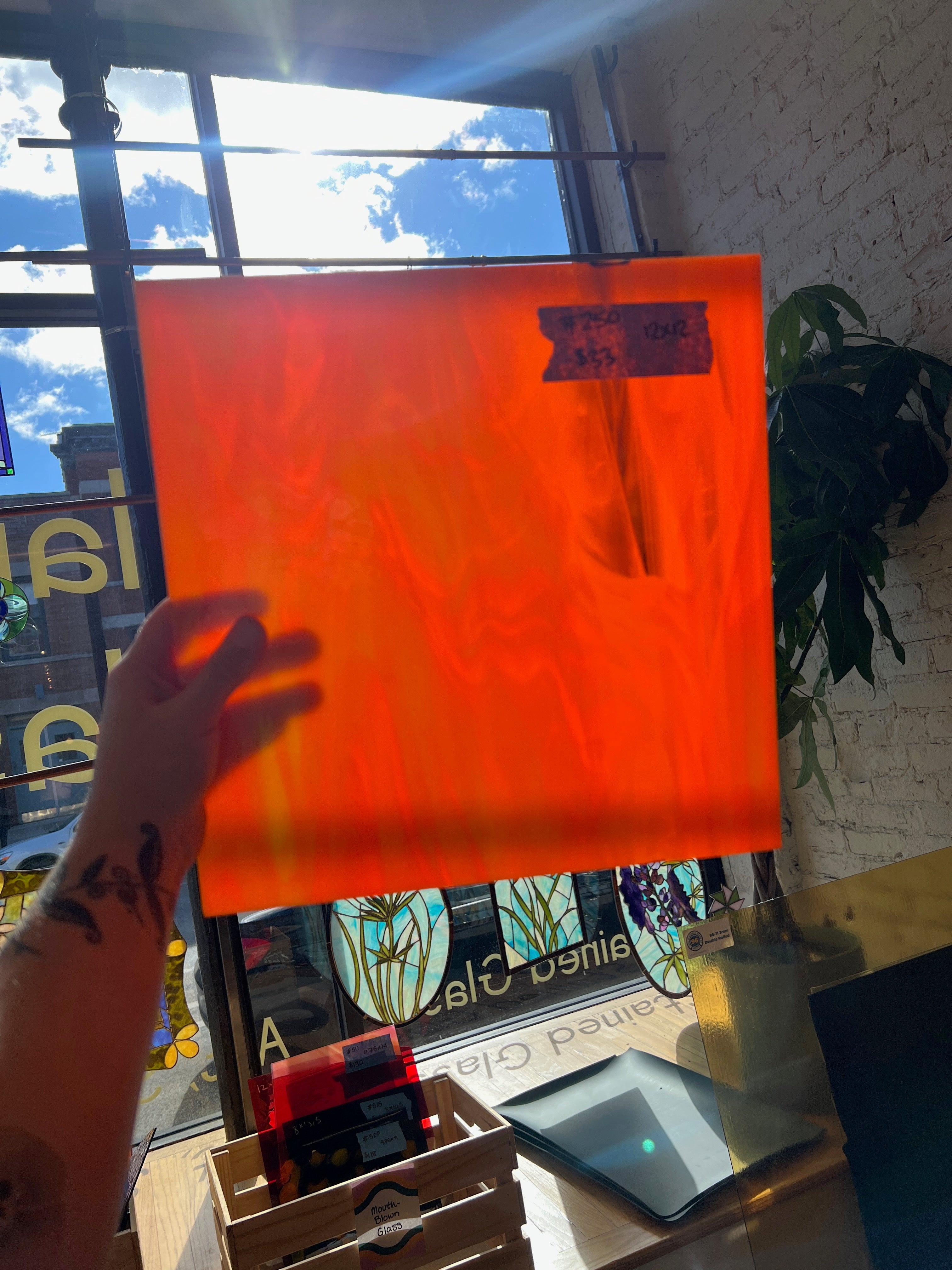 Person holding an orange swirled sheet of glass in front of a window with stained glass