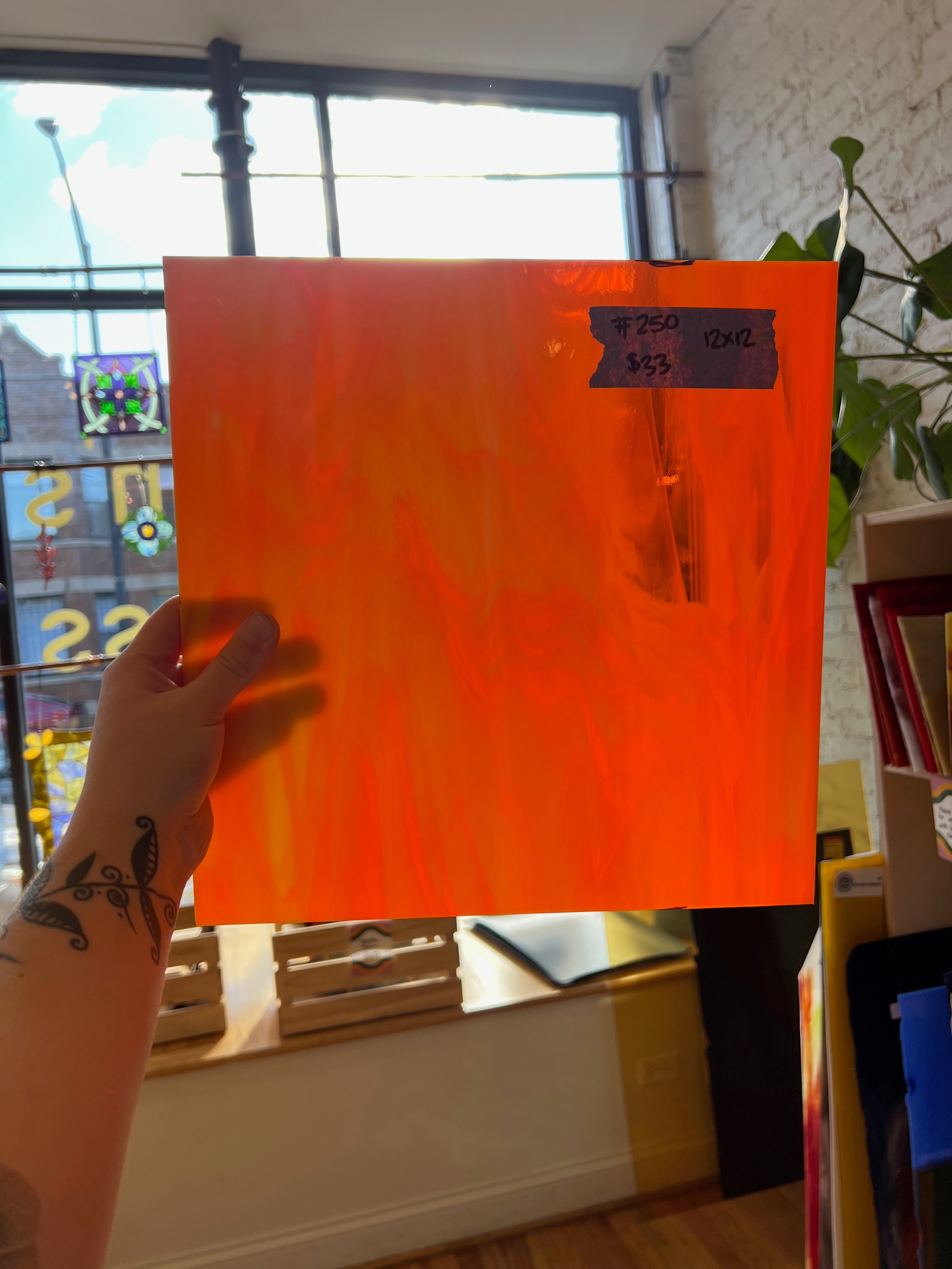 Hand holding an orange sheet of glass with text in a room with a window and books.