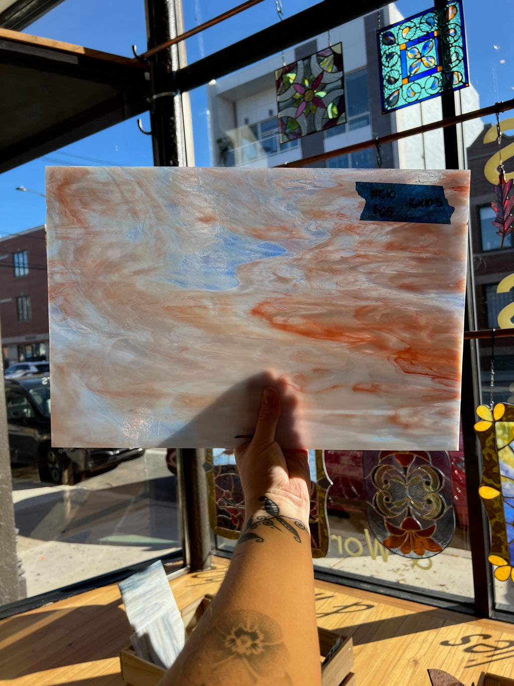 Person holding a marbled piece of glass in front of a store window with stained glass.