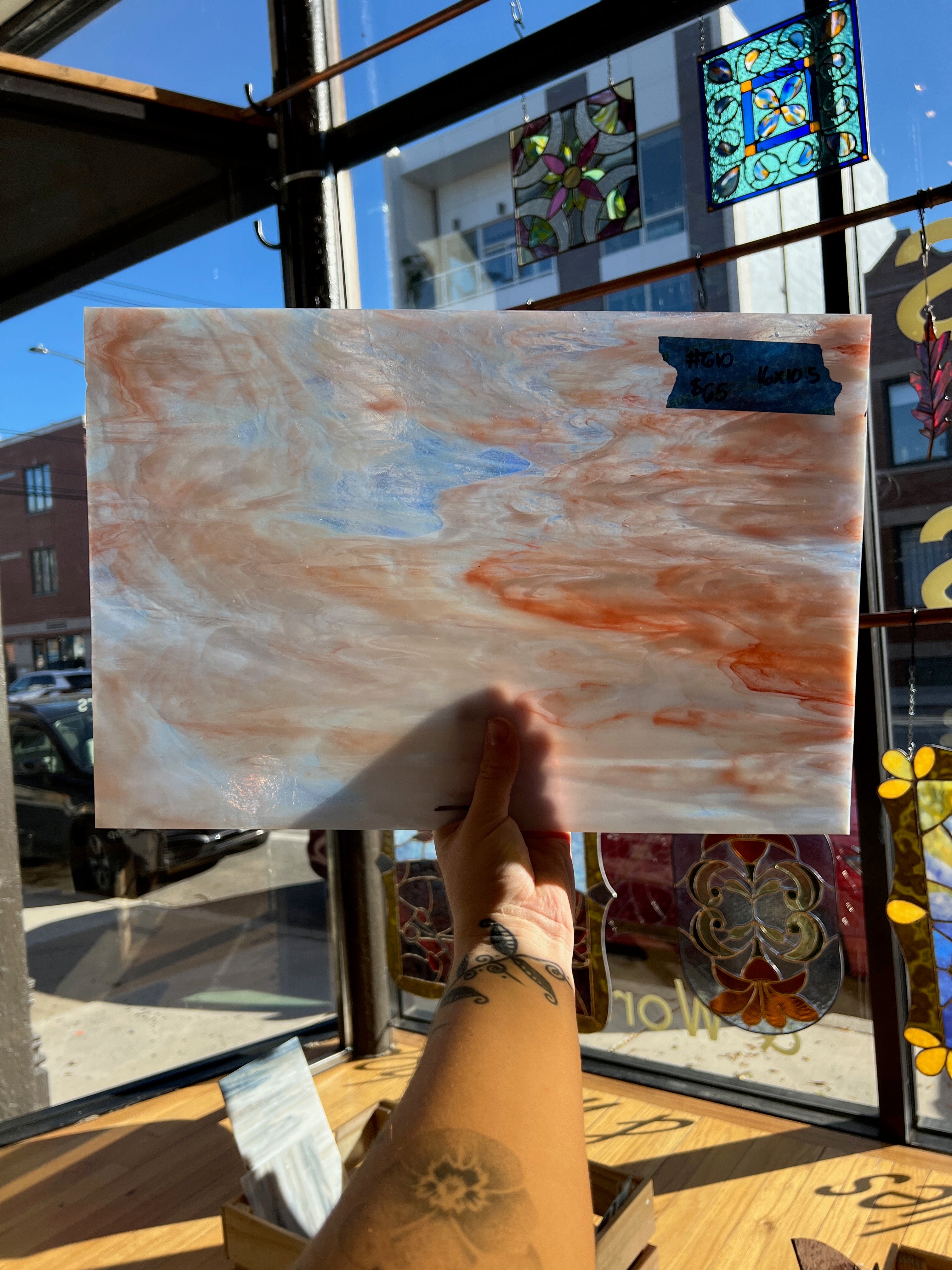 Person holding a marbled piece of glass in front of a store window with stained glass.