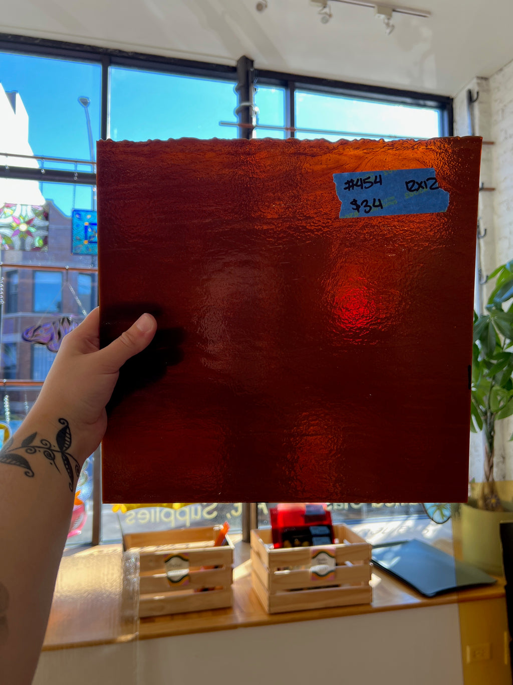 Red textured piece of stained glass held by a person indoors with a window in the background