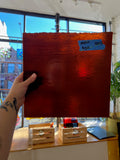 Red textured piece of stained glass held by a person indoors with a window in the background