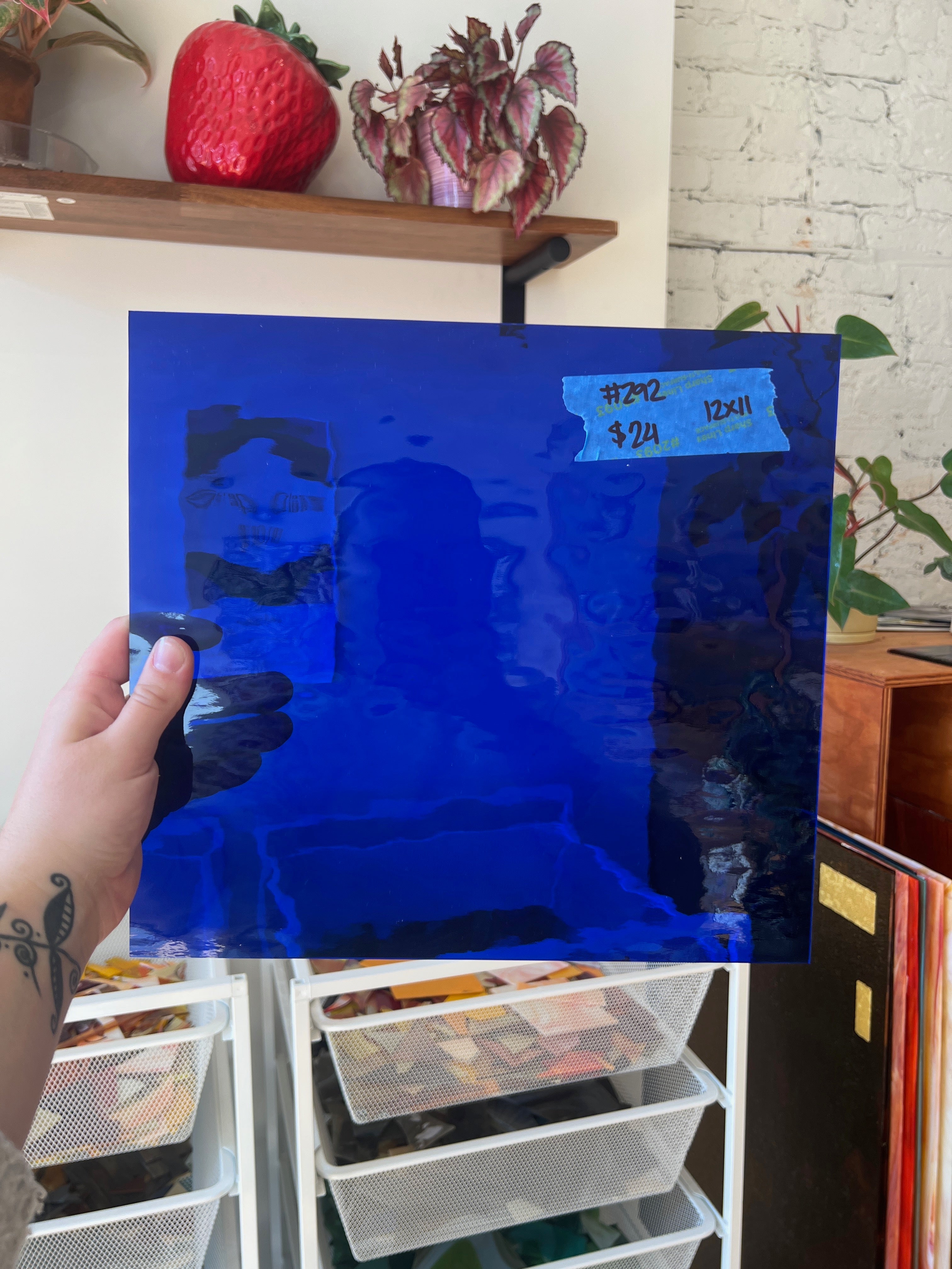 Person holding a blue piece of glass with visible text and images on a shelf.