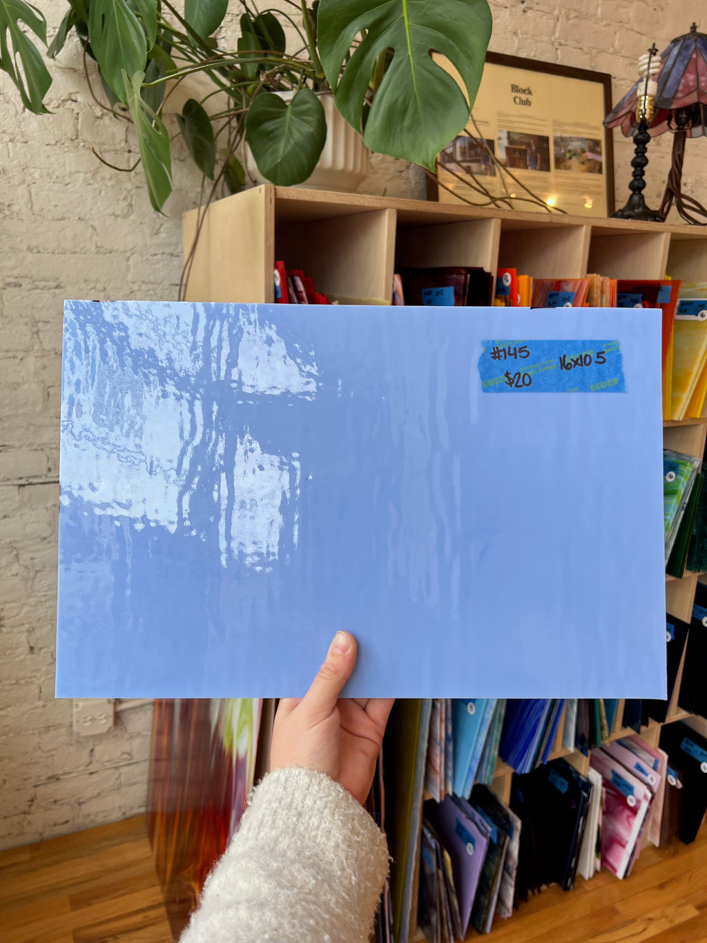Blue piece of stained glass held by a person in front of a bookshelf with various items.