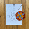 Decorative geometric stained glass panel on a wooden surface with a paper featuring a design diagram.