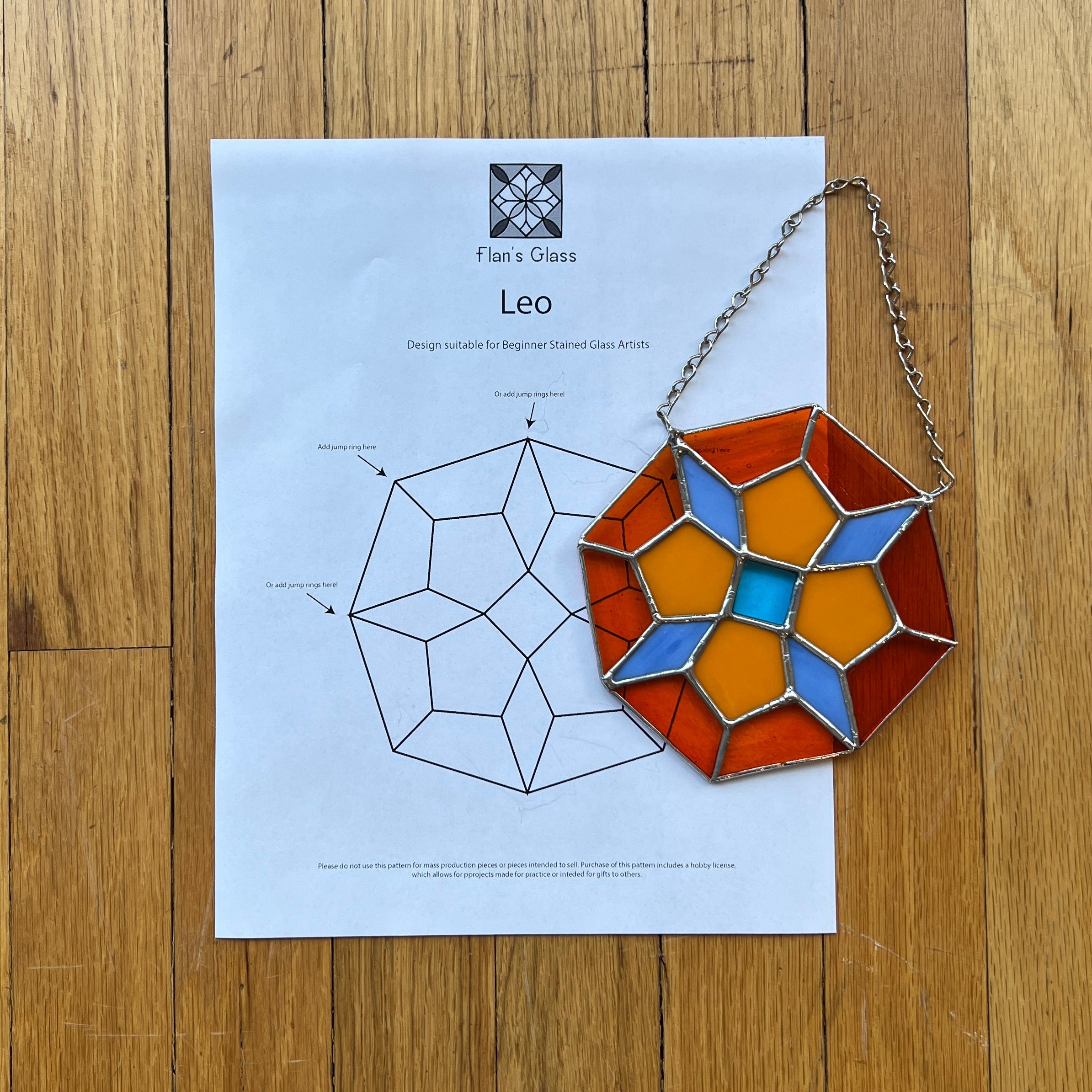 Decorative geometric stained glass panel on a wooden surface with a paper featuring a design diagram.