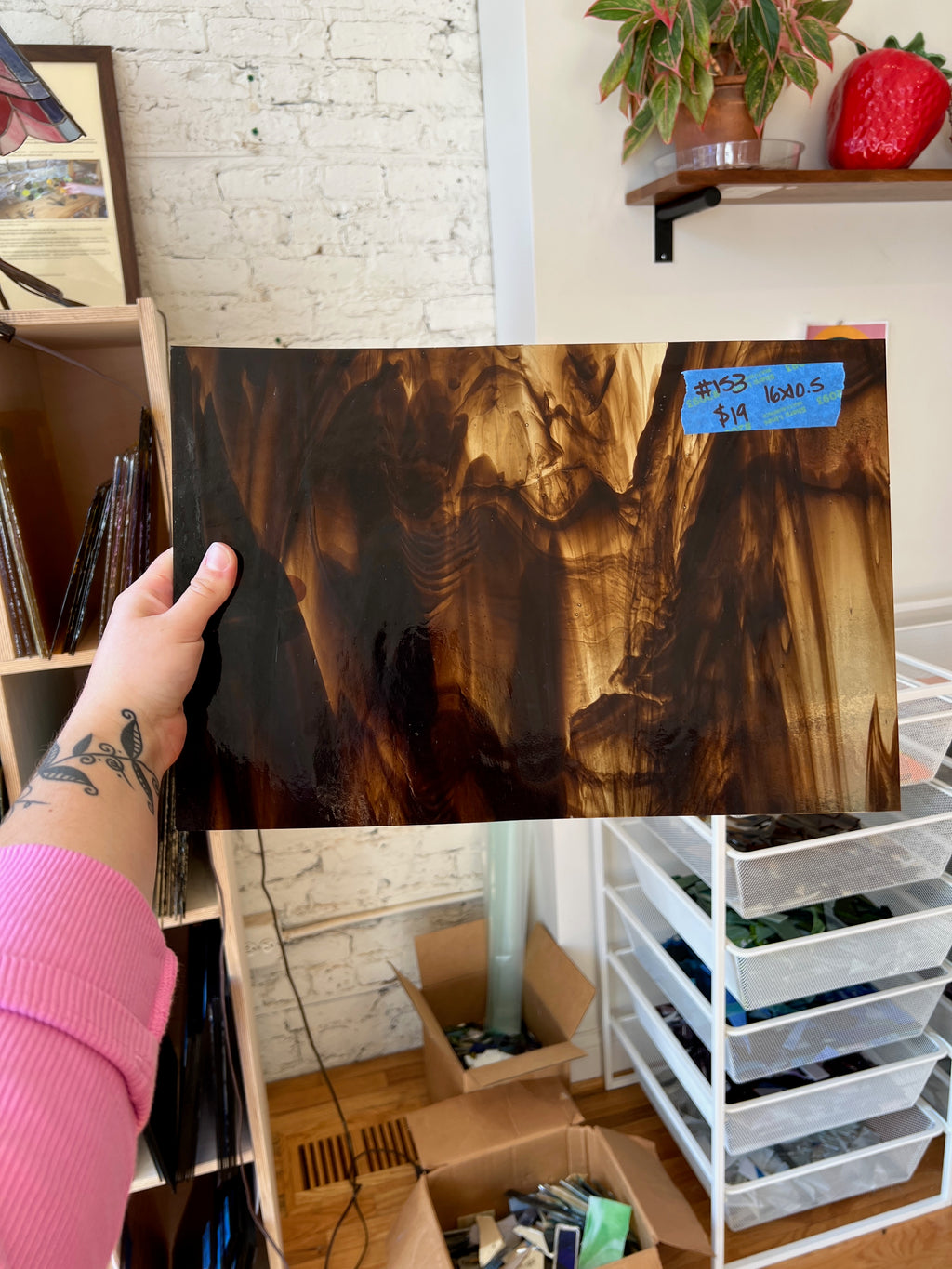 Person holding a large piece of brown swirled stained glass with a textured surface in a room with shelves and boxes.