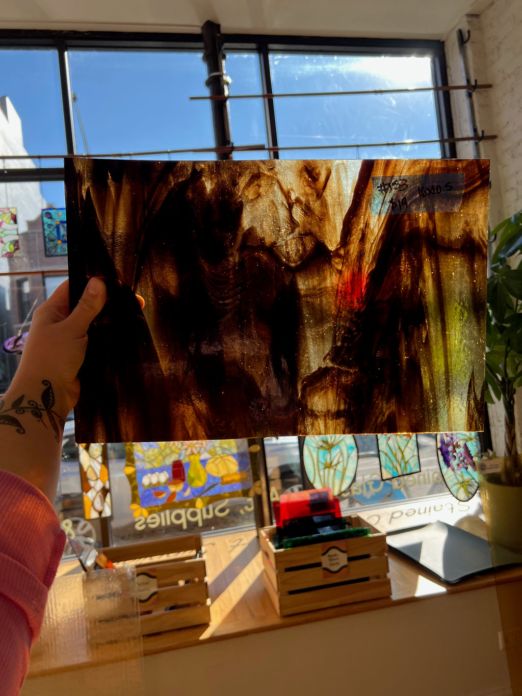 Person holding a piece of brownish stained glass in front of a window with stained glass