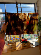 Person holding a piece of brownish stained glass in front of a window with stained glass