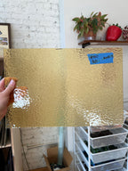 Gold textured glass sheet held up with a blurred indoor background