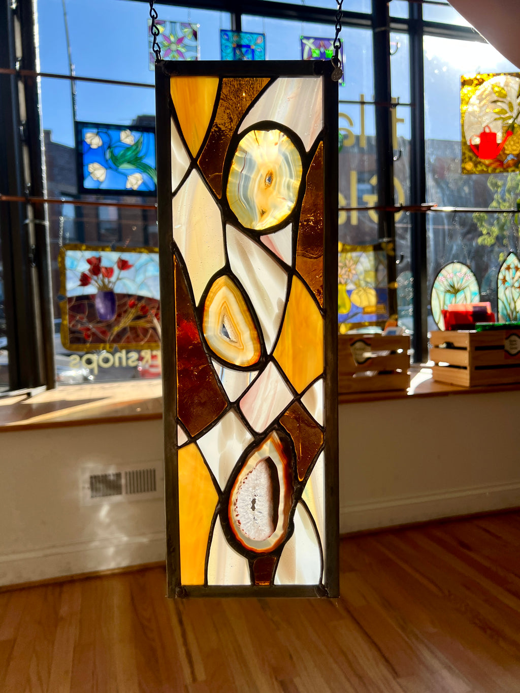 Stained glass panel with abstract design in a room with other artworks on the wall.