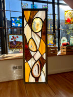 Stained glass panel with abstract design in a room with other artworks on the wall.
